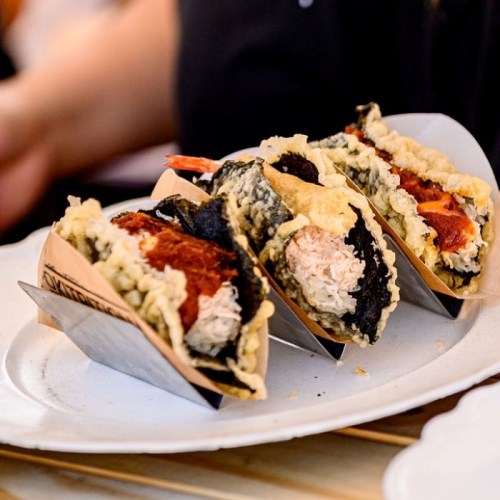 Three crispy tacos filled with seafood and topped with various ingredients, served on a white plate.