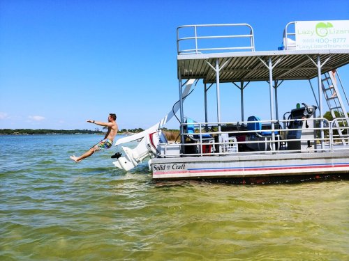 A person jumps off the side of a boat into the water on a sunny day.