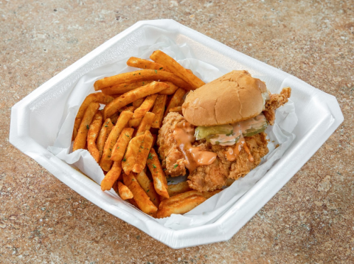 A crispy fried chicken sandwich with pickles and sauce, served with a side of golden sweet potato fries.