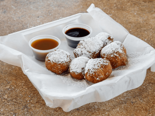 A tray of powdered sugar-dusted doughnuts with two dipping sauces on the side.