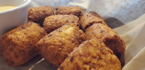 A close-up of golden-brown, crispy fried snacks served with a small bowl of dipping sauce.