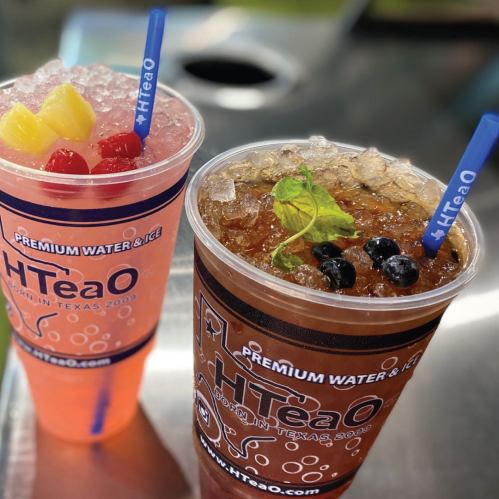 Two colorful drinks in clear cups, one pink with fruit and the other brown with mint and berries, on a table.