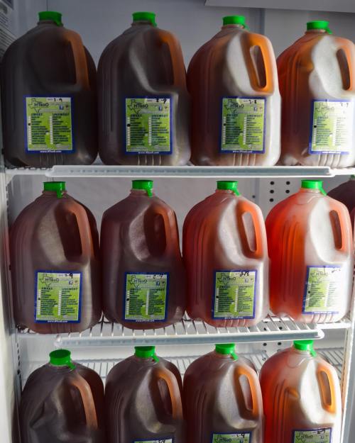A refrigerator shelf filled with multiple jugs of iced tea, each with a green cap and a label on the front.