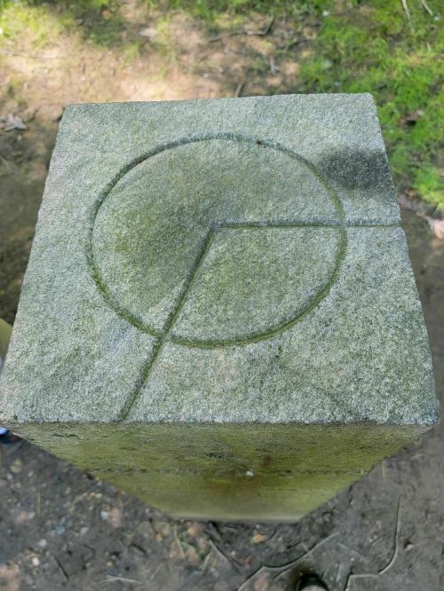 Top view of a stone pillar featuring a carved circular design and geometric lines on its surface.