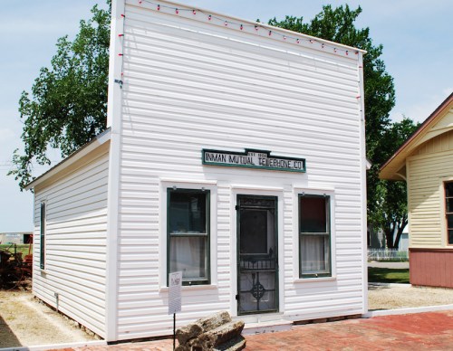 Historic white building with a sign reading "Inman Mutual Telephone Co." and a front door, surrounded by greenery.