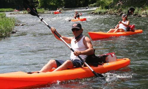 A group of people kayaking on a river in bright orange kayaks on a sunny day.