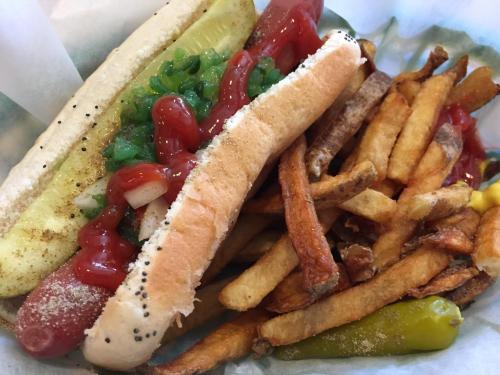 A hot dog topped with ketchup, onions, and pickles, served with a side of crispy French fries.