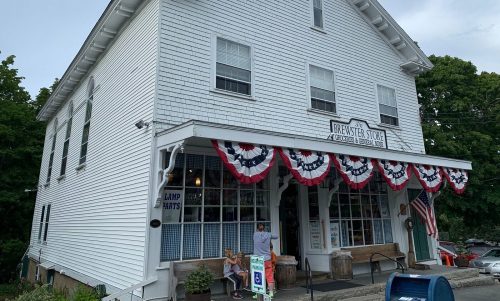 A white, two-story building with red, white, and blue bunting, featuring a sign that reads "Brewster Store."