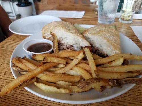 A plate with a sandwich cut in half, served with a side of fries and a small cup of dipping sauce.