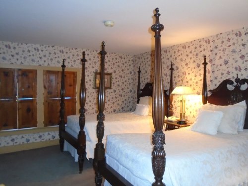 A cozy bedroom with two four-poster beds, floral wallpaper, and a warm lamp illuminating the space.