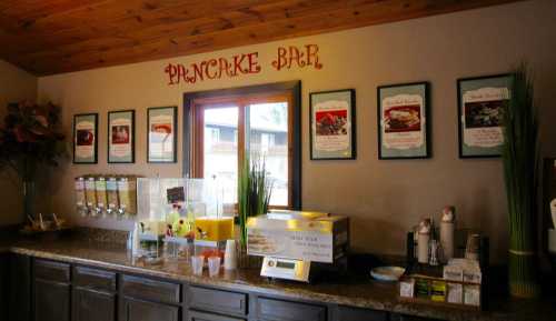 A cozy pancake bar with a wooden ceiling, framed menus on the wall, and a counter with syrup dispensers and condiments.