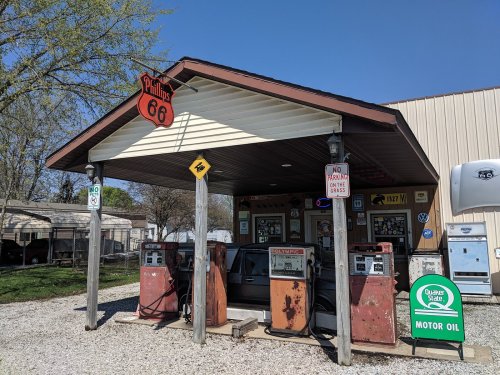 A vintage gas station with old pumps under a roof, featuring a Route 66 sign and a motor oil advertisement.