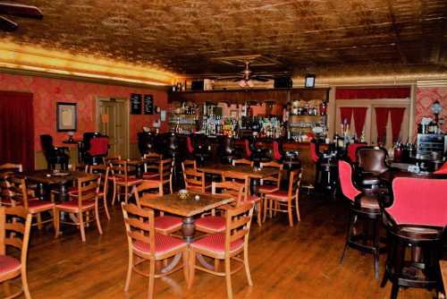 Cozy bar interior with wooden tables, red upholstered chairs, and a well-stocked bar against a patterned wall.