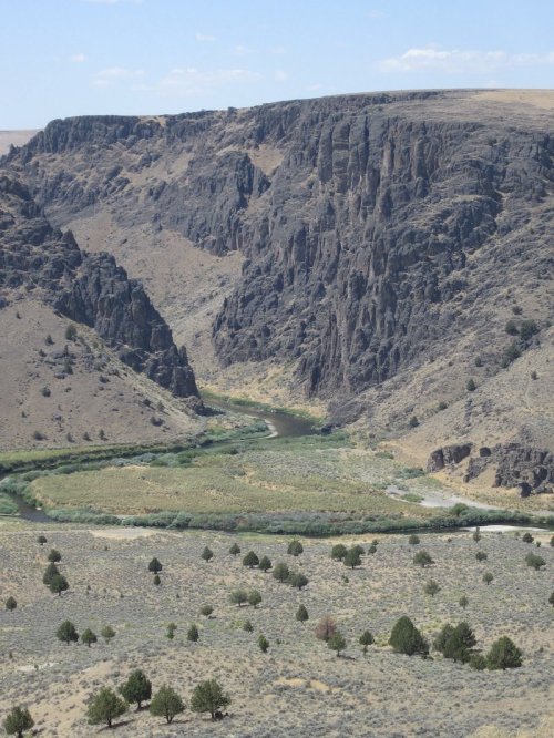 A winding river flows through a rocky canyon surrounded by dry hills and sparse vegetation under a blue sky.