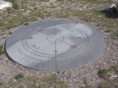 A circular stone compass rose embedded in the ground, surrounded by grass and gravel.