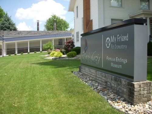 Sign for "My Friend Pet Memorialary" and "Famous Endings Museum" in a grassy area with a building in the background.