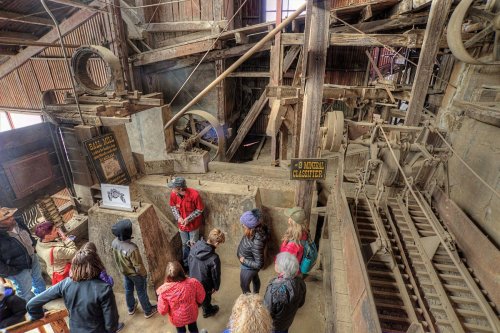 A group of people listens to a guide in a dusty, old industrial building filled with machinery and wooden structures.