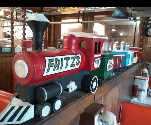 A colorful wooden toy train with "Fritz's" on the engine, displayed on a counter in a cozy restaurant.