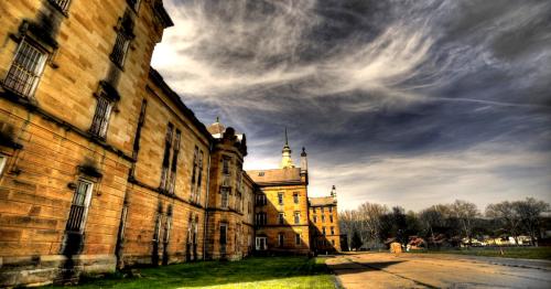 Historic stone building under a dramatic sky, featuring intricate architecture and a grassy foreground.