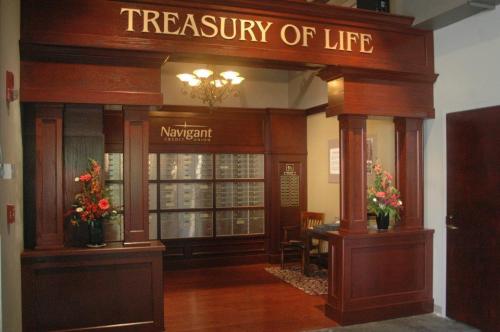 Interior of a wooden reception area labeled "Treasury of Life," featuring floral arrangements and a display board.