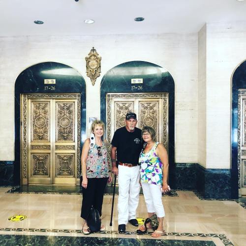 Three people stand in front of ornate elevator doors in a stylish lobby, smiling and posing for the photo.