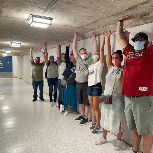 A group of people stands in a hallway, raising their arms in celebration, all wearing masks.