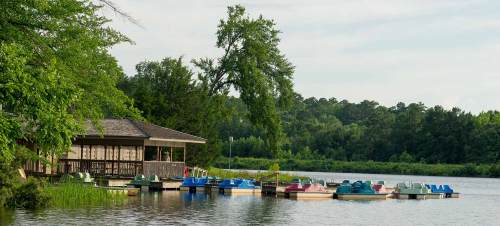 A serene lake scene with a wooden dock, colorful paddle boats, and lush greenery in the background.