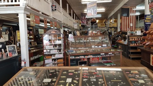Interior of a vintage store featuring display cases, shelves of merchandise, and historical signage.