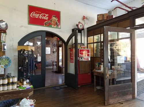 Interior of a vintage store featuring a Coca-Cola sign, wooden doors, and various nostalgic items on display.