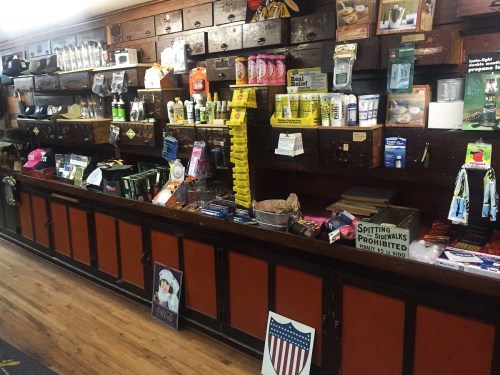 A rustic store display featuring various products, including tools, snacks, and souvenirs, against wooden shelves.