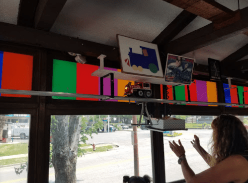 A colorful window display with a toy truck and framed art, while a person gestures enthusiastically nearby.