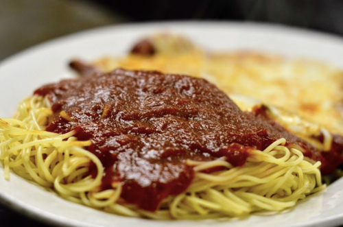 A plate of spaghetti topped with marinara sauce, served alongside a cheesy baked dish.