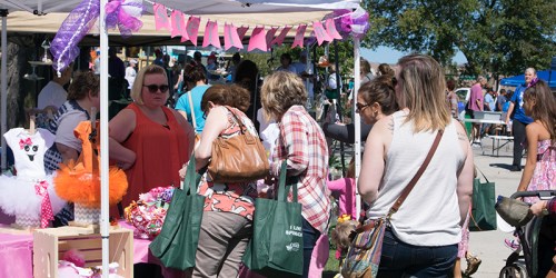 A busy outdoor market scene with people browsing colorful vendor stalls under tents.