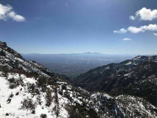 A panoramic view of snow-capped mountains overlooking a vast valley under a clear blue sky.