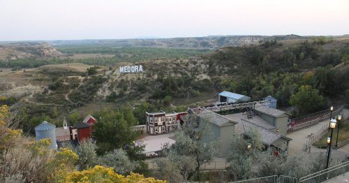 A scenic view of Medora, North Dakota, featuring the town's name on a hillside and surrounding green landscapes.