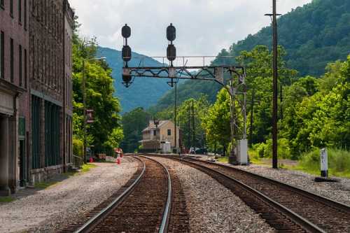 A view of a railway track curving through a green landscape, with a signal tower and buildings in the background.