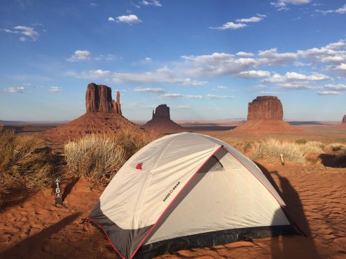 A tent set up in a desert landscape with red rock formations and a blue sky dotted with clouds.