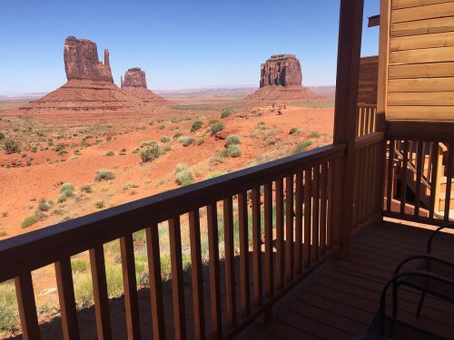 View from a wooden balcony overlooking red rock formations and desert landscape under a clear blue sky.