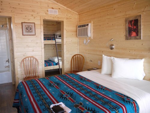 Cozy wooden room with a double bed, bunk beds, and air conditioning, featuring a colorful patterned blanket.