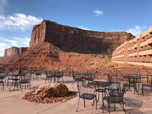A patio with black metal tables and chairs overlooks a red rock formation under a blue sky.