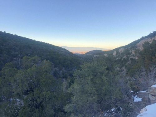 A scenic view of a valley surrounded by mountains, with trees and a clear sky at dusk.