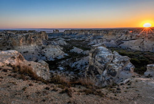 Sunset over a rugged canyon landscape, highlighting rocky formations and a vast, open sky.