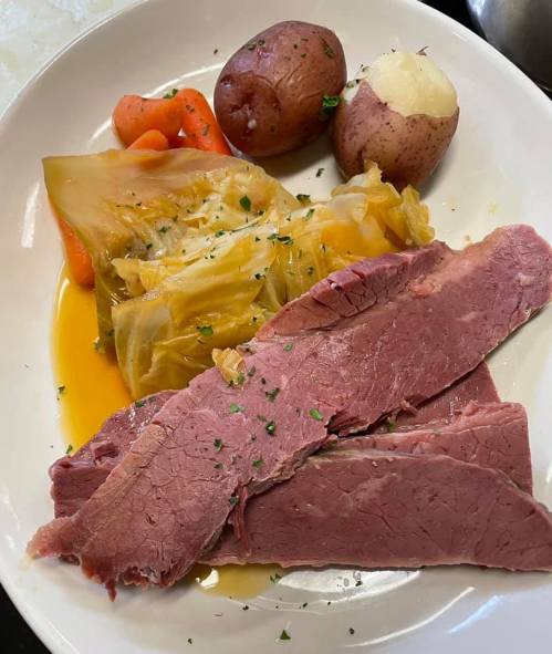 A plate of corned beef, cabbage, carrots, and potatoes, garnished with herbs.