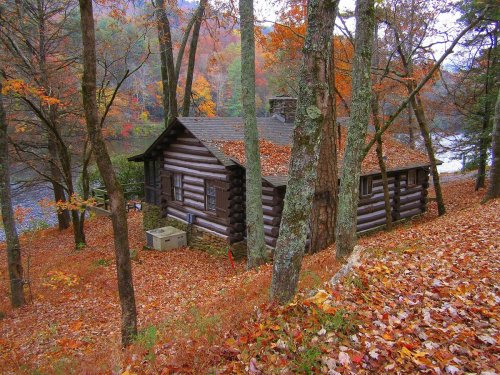 A cozy log cabin surrounded by colorful autumn foliage near a serene lake.
