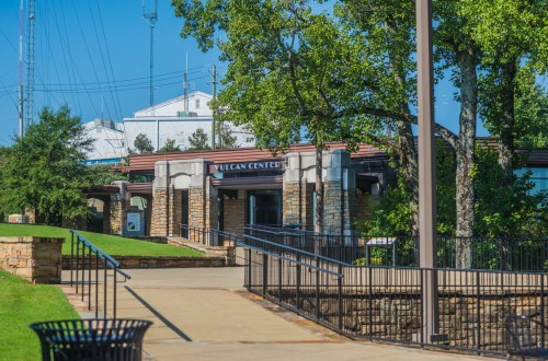 Vulcan Center entrance with stone architecture, surrounded by trees and a clear blue sky. Pathway leads to the building.
