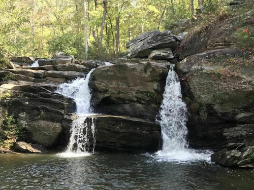 A serene waterfall cascading over rocks into a calm pool, surrounded by lush green trees.