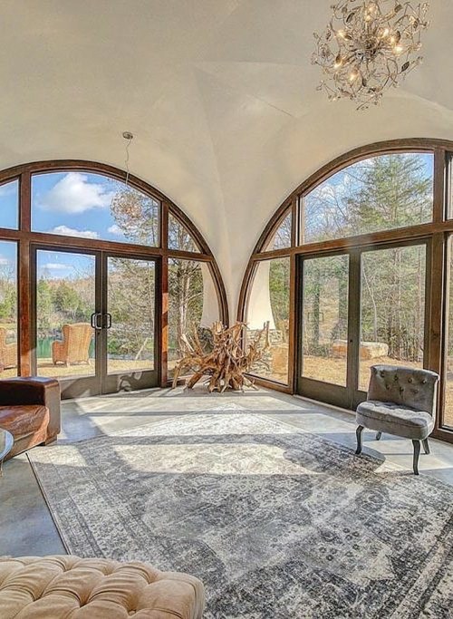 Bright, modern interior with large arched windows, a cozy rug, and stylish furniture, surrounded by nature.