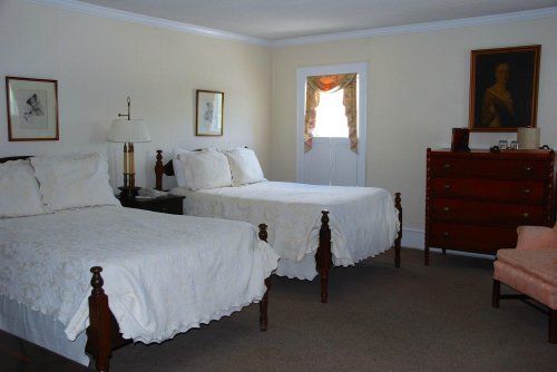 A cozy bedroom featuring two beds with white bedding, a dresser, and soft lighting from a window.