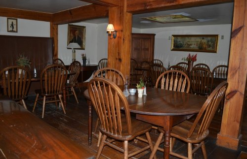 Cozy dining room with wooden tables and chairs, featuring warm lighting and decorative artwork on the walls.