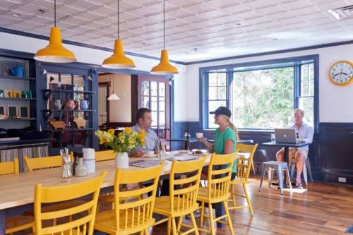 A bright café with yellow chairs, two people chatting at a table, and another person working on a laptop by the window.